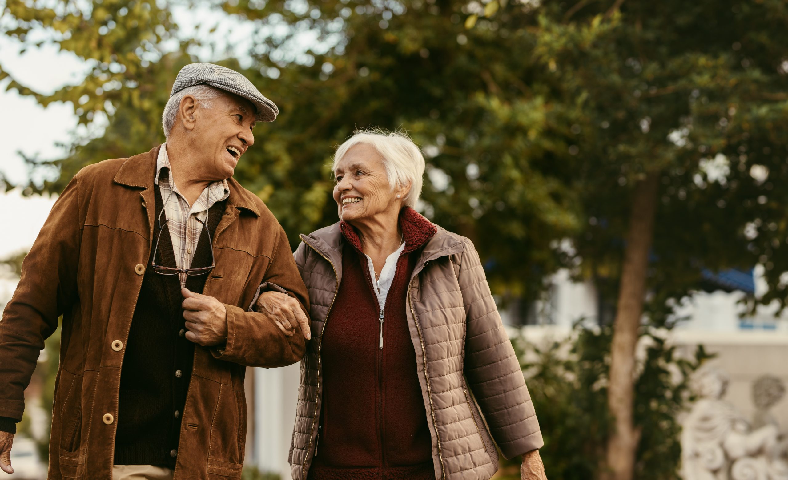 A senior man and woman hold hands while walking on a cool day.