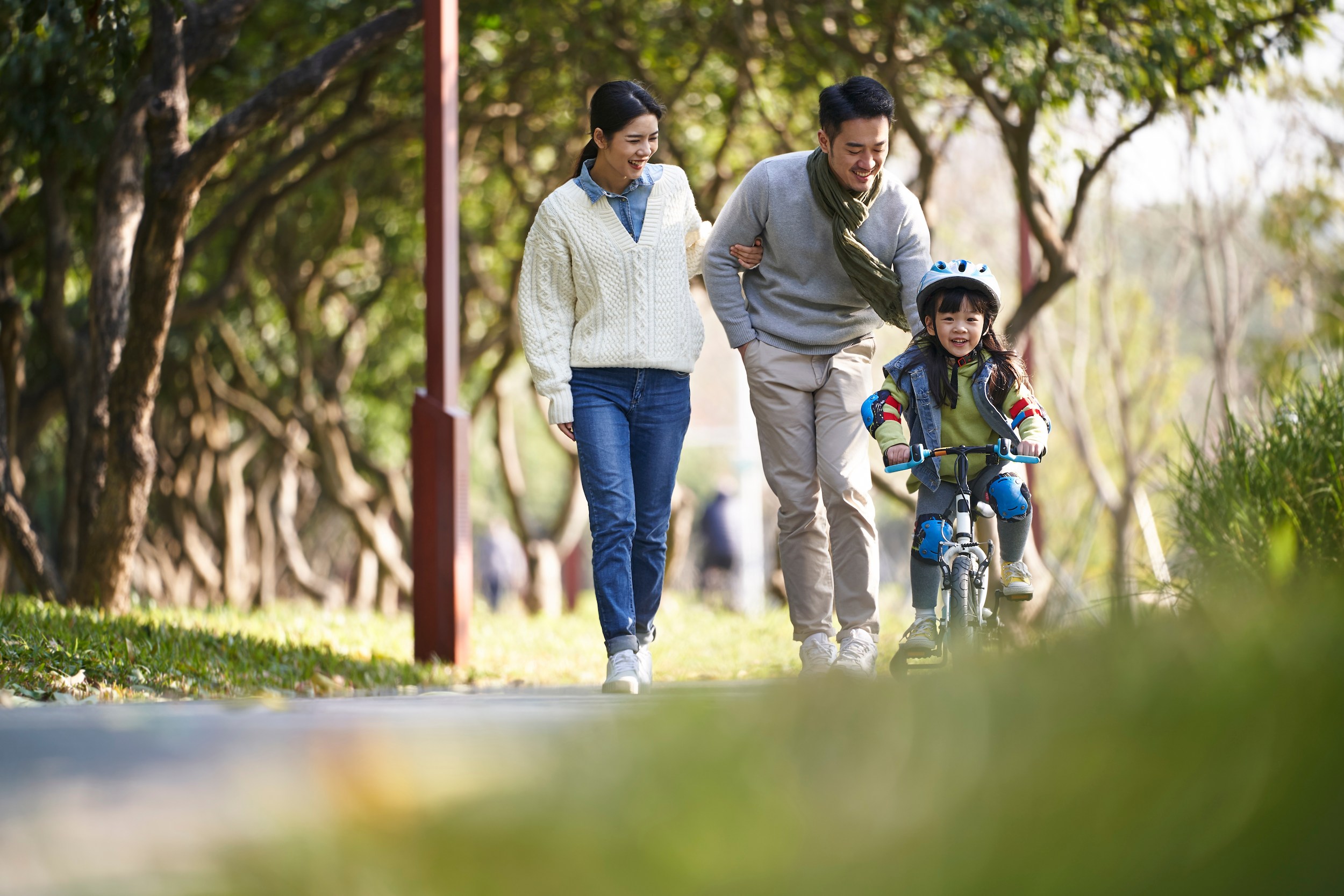 Young family teaching their daughter to ride a bicycle in the park