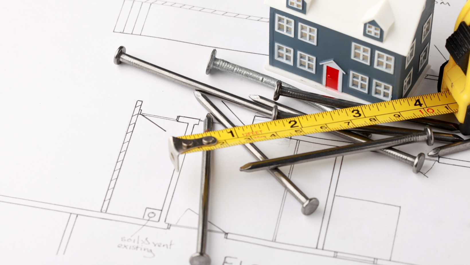 Nails, tape measure, and small model home sit atop a blueprint.