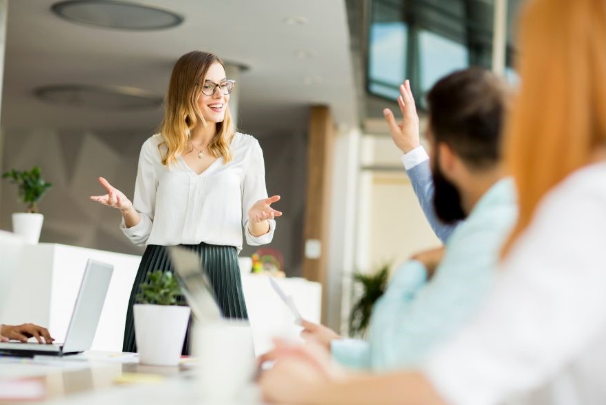 person presenting to a table of people with one person raising their hand