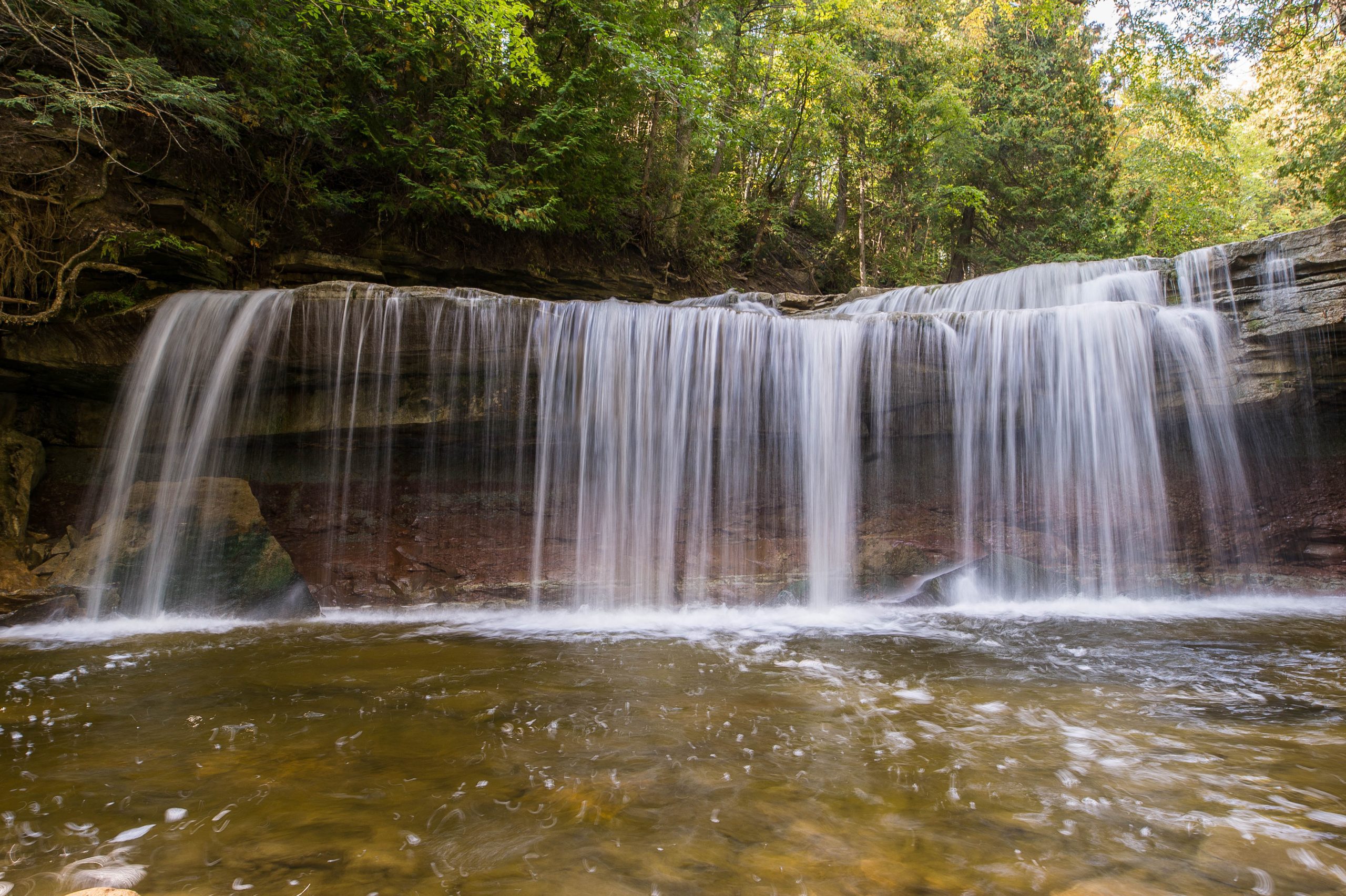 A small waterfall flows over a rocky bank into a stream below.