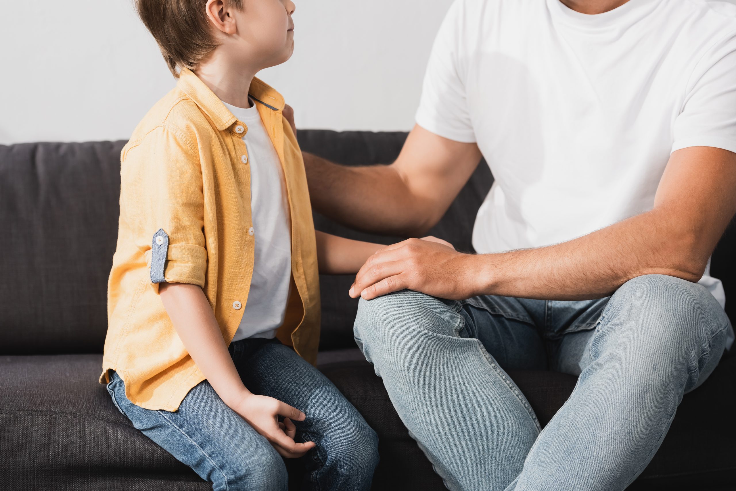 An adult and child sit on a couch together.