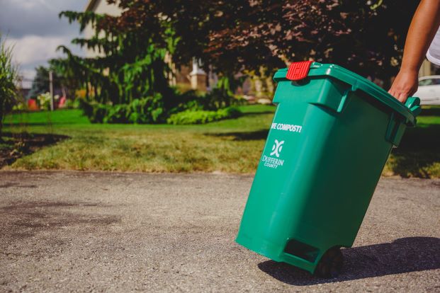 green bin being pulled up an asphalt driveway