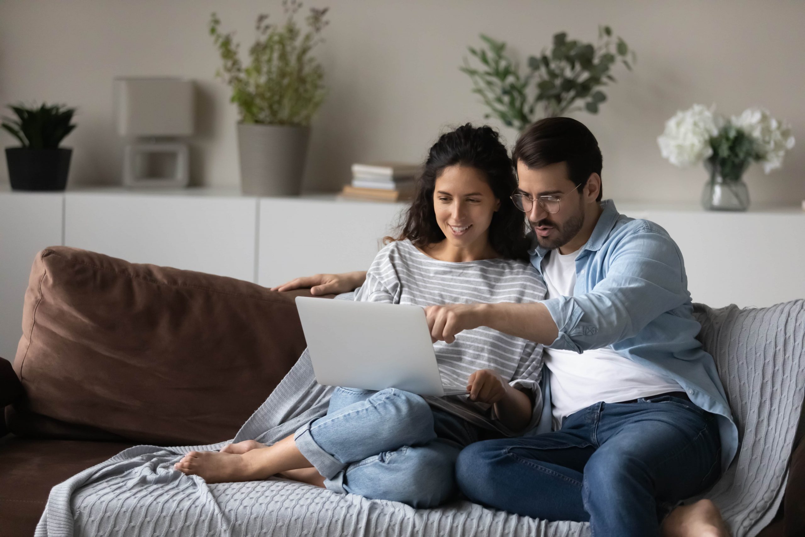 A young couple sit on couch looking at laptop screen